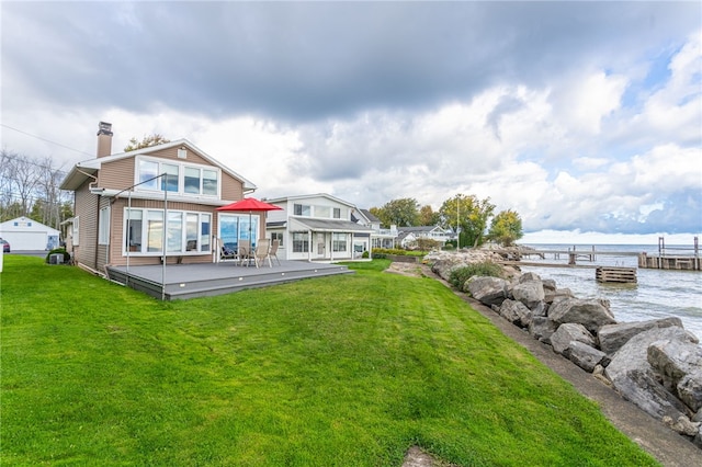 rear view of property featuring a lawn, a chimney, and a deck with water view