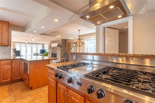 kitchen with a stone fireplace, brown cabinetry, stainless steel appliances, range hood, and light stone countertops