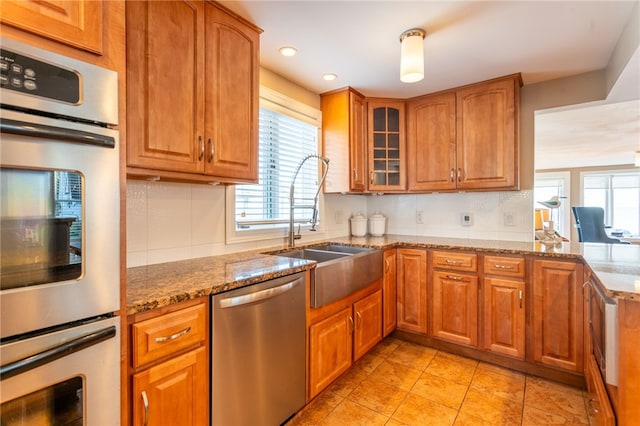 kitchen with a sink, brown cabinetry, decorative backsplash, stainless steel appliances, and light stone countertops
