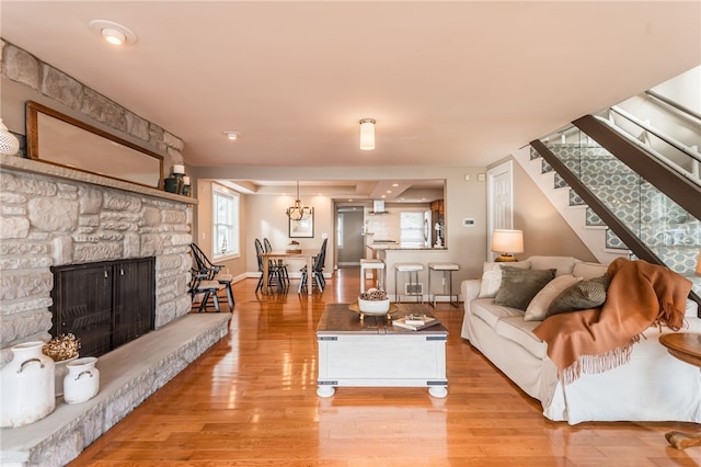 living area with wood finished floors, a stone fireplace, baseboards, and stairway