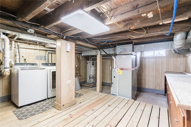 basement featuring water heater, heating unit, washer and clothes dryer, wooden walls, and light wood-style floors