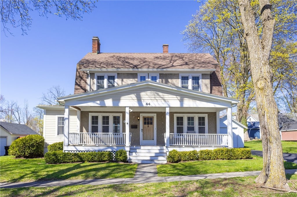 view of front of house featuring a chimney, covered porch, and a front yard