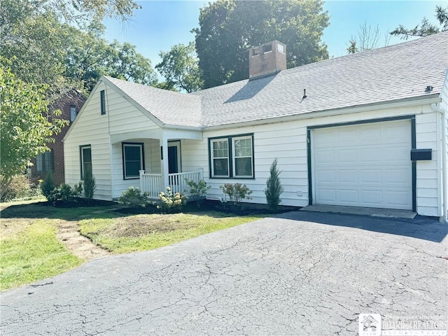 ranch-style home featuring a chimney, a shingled roof, an attached garage, driveway, and covered porch