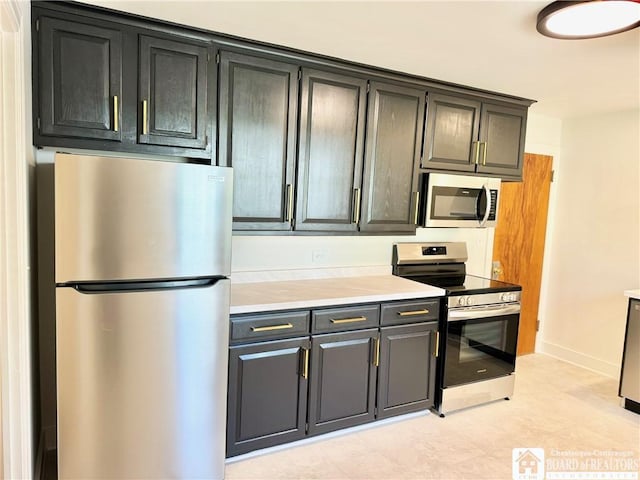 kitchen with baseboards, appliances with stainless steel finishes, dark cabinetry, and light countertops