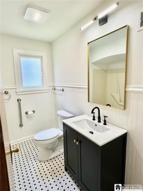 half bath featuring wainscoting, vanity, tile patterned flooring, and toilet