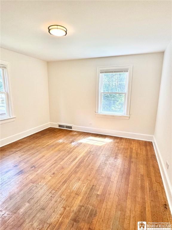 unfurnished room with wood-type flooring, baseboards, a healthy amount of sunlight, and visible vents