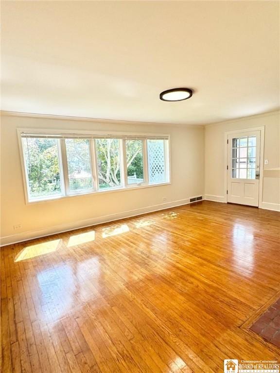 empty room with hardwood / wood-style floors, visible vents, and baseboards