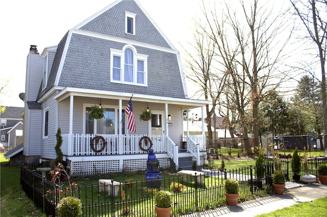 view of front of property with a gambrel roof, covered porch, a front yard, and roof with shingles