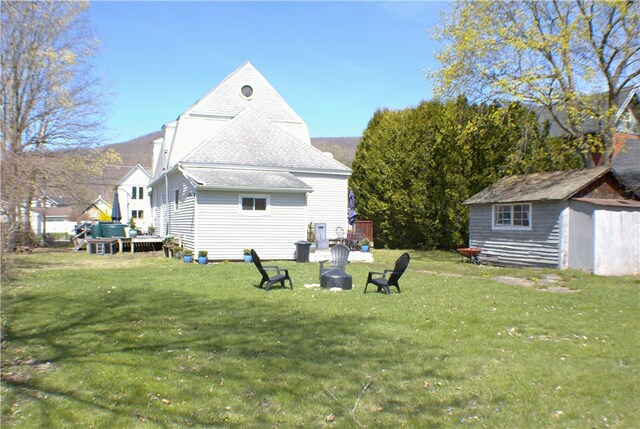 rear view of property with a storage unit, roof with shingles, an outbuilding, and a lawn