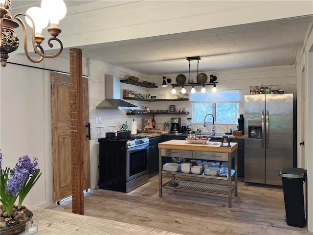 kitchen with wall chimney range hood, dark countertops, open shelves, stainless steel appliances, and light wood finished floors