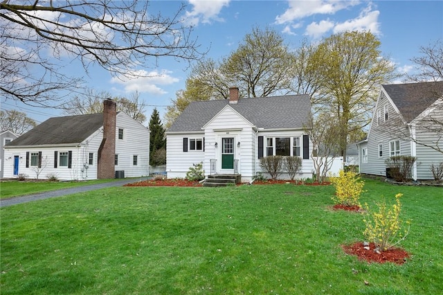 view of front of house featuring roof with shingles, a front lawn, central AC, a chimney, and entry steps