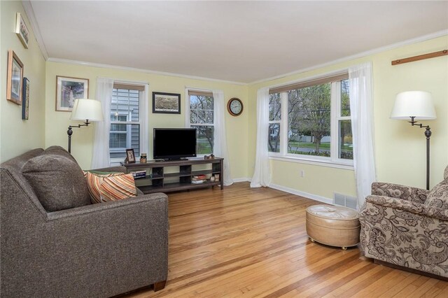 living area featuring light wood-style floors, visible vents, baseboards, and ornamental molding
