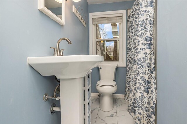 bathroom with marble finish floor, toilet, curtained shower, and baseboards
