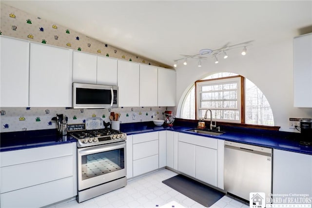 kitchen featuring a sink, dark countertops, white cabinetry, rail lighting, and appliances with stainless steel finishes