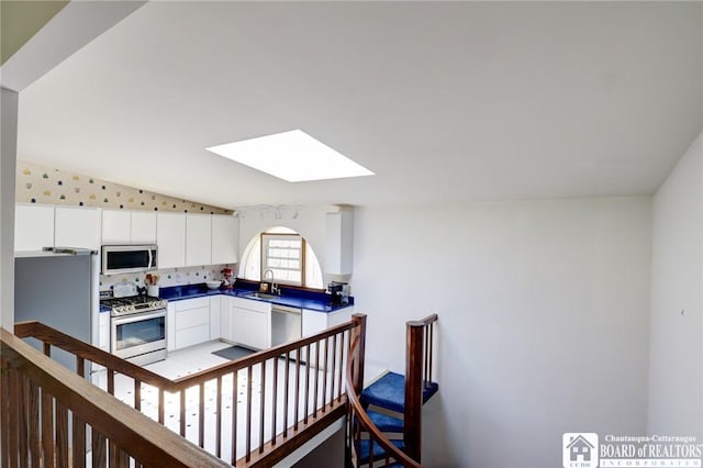 kitchen featuring white cabinets, dark countertops, a sink, vaulted ceiling with skylight, and appliances with stainless steel finishes