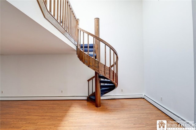 staircase featuring a baseboard heating unit and wood finished floors