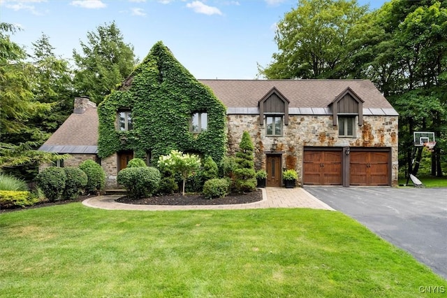 tudor house with a front lawn, driveway, stone siding, and a garage