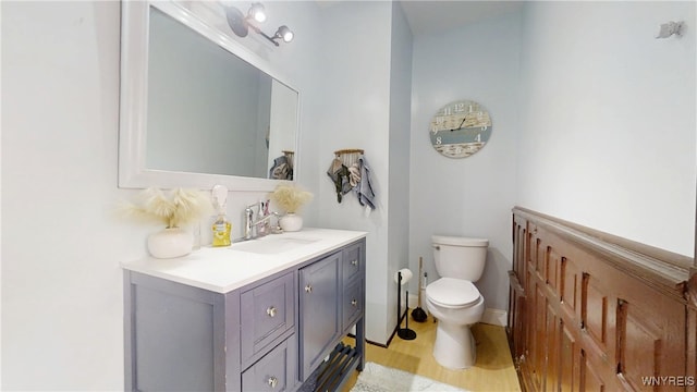 half bath featuring wood finished floors, toilet, and vanity