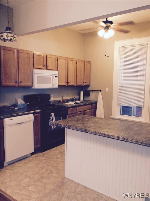 kitchen featuring dark countertops, hanging light fixtures, a ceiling fan, and white appliances