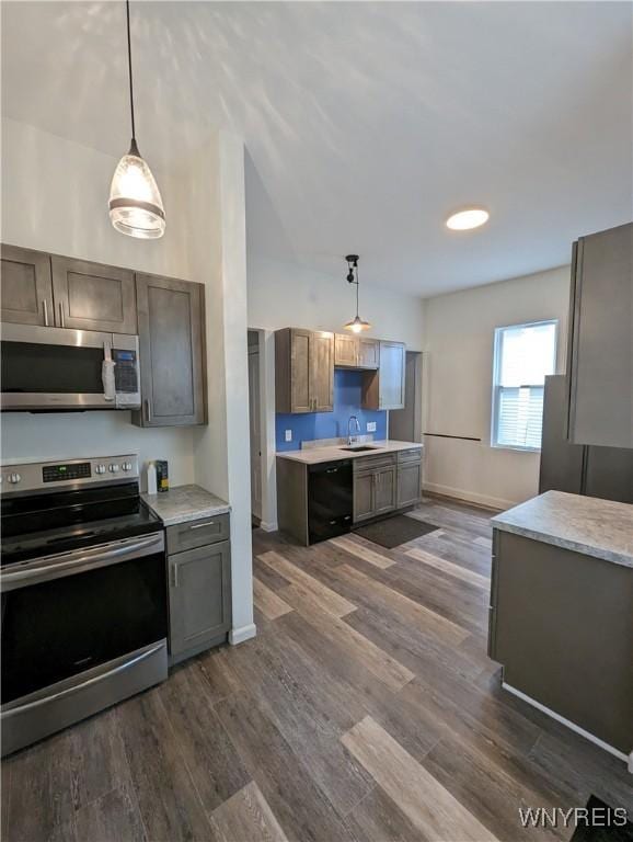kitchen with a sink, stainless steel appliances, light countertops, decorative light fixtures, and dark wood-style floors