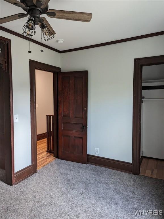 unfurnished bedroom featuring ceiling fan, baseboards, light colored carpet, and crown molding
