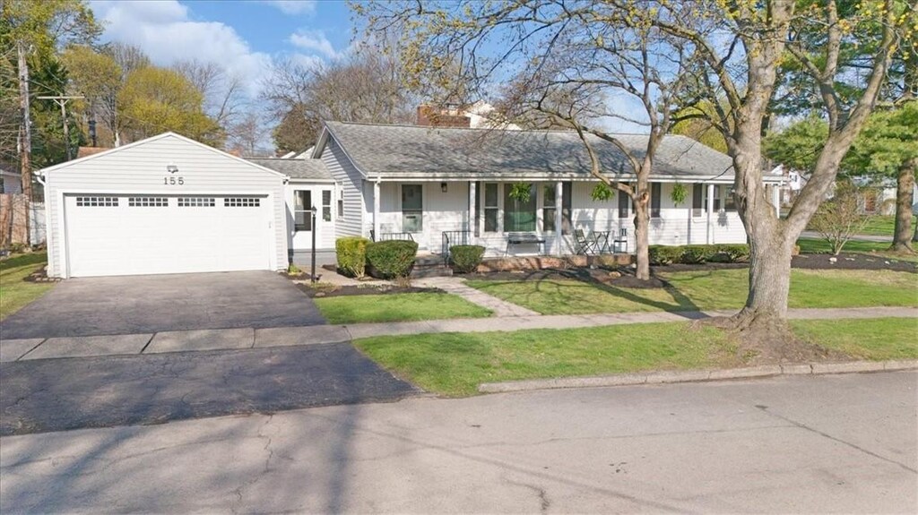ranch-style home with driveway, a porch, a chimney, an attached garage, and a front yard