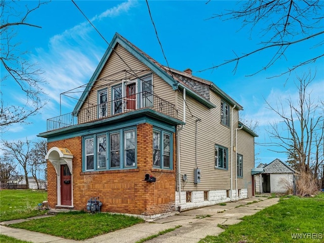 view of front facade featuring a chimney, a front lawn, brick siding, and a balcony