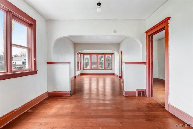 corridor featuring visible vents, baseboards, arched walkways, and wood-type flooring