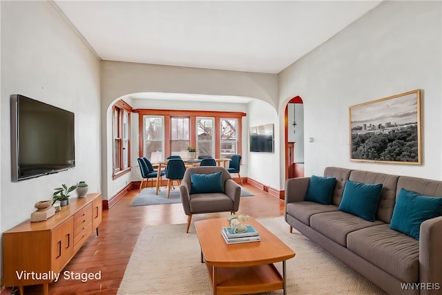 living area with arched walkways, light wood-type flooring, and baseboards