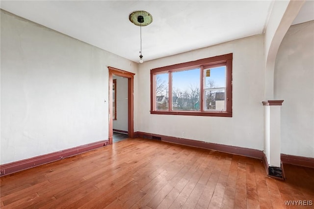 empty room featuring hardwood / wood-style flooring, baseboards, and arched walkways