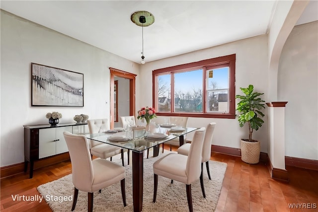 dining room with arched walkways, light wood finished floors, and baseboards