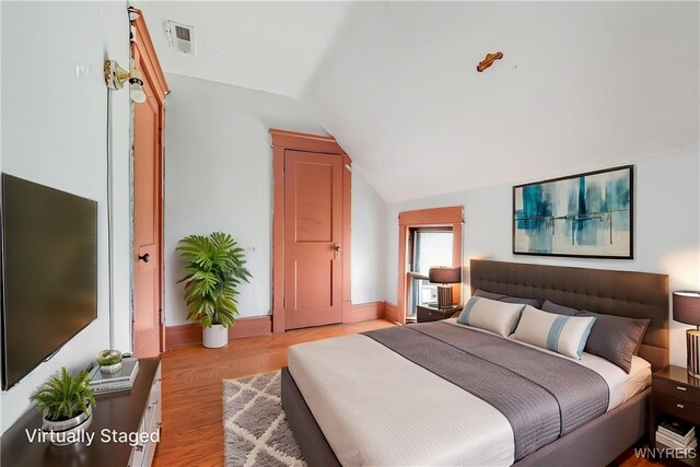 bedroom with vaulted ceiling, visible vents, baseboards, and light wood-type flooring