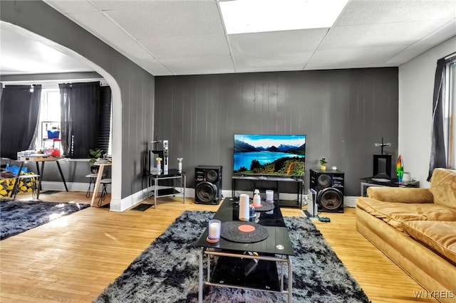 living room with arched walkways, wood finished floors, a drop ceiling, and baseboards