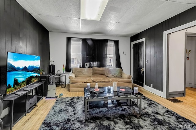 living area with a paneled ceiling, wood walls, light wood finished floors, and baseboards