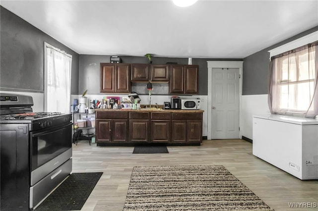 kitchen with light wood-type flooring, plenty of natural light, gas stove, and white microwave