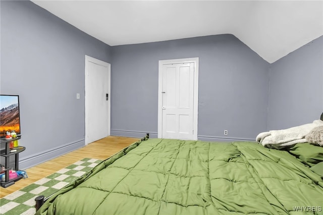 bedroom featuring wood finished floors, lofted ceiling, and baseboards