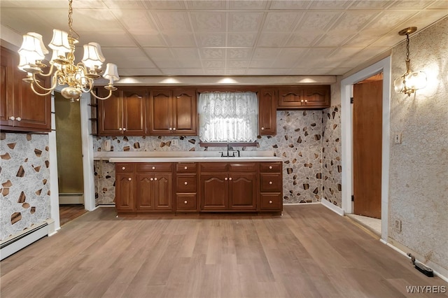 kitchen with a baseboard heating unit, light countertops, an inviting chandelier, and light wood-style floors