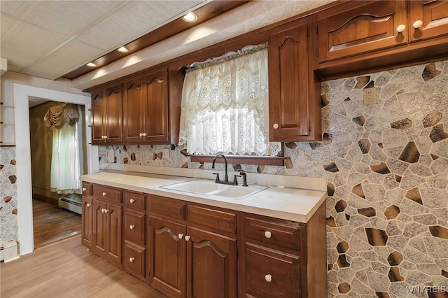 kitchen with light countertops, light wood-type flooring, baseboard heating, and a sink