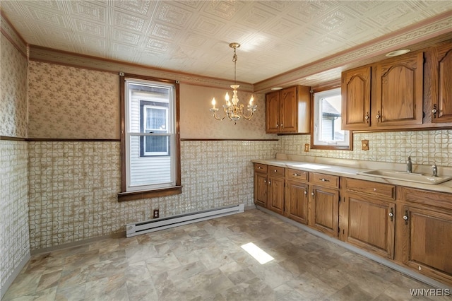 kitchen with a sink, a baseboard heating unit, brown cabinetry, a chandelier, and light countertops