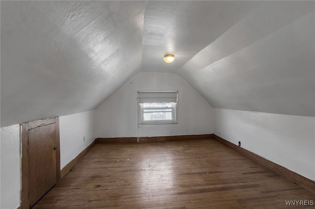 additional living space with wood-type flooring, vaulted ceiling, a textured ceiling, and baseboards