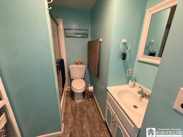 bathroom with toilet, walk in shower, vanity, and wood finished floors