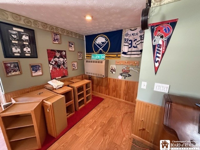 rec room featuring wood finished floors, a textured ceiling, wood walls, and a wainscoted wall