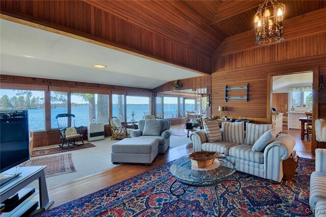living area with a water view, a chandelier, wood finished floors, wood walls, and wooden ceiling