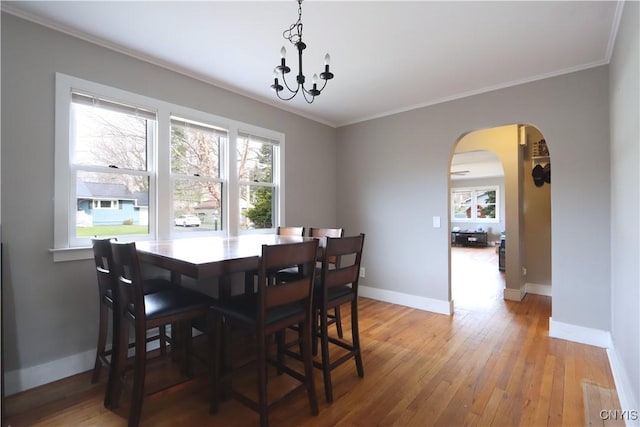 dining area with arched walkways, light wood-style flooring, ornamental molding, baseboards, and a notable chandelier