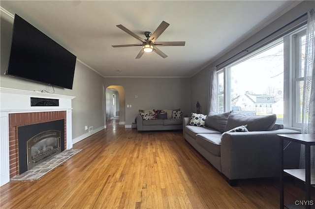 living area with arched walkways, light wood-style floors, a brick fireplace, and a ceiling fan