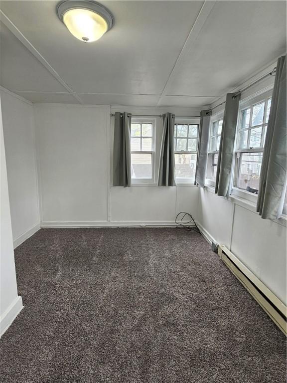 empty room with a baseboard heating unit, plenty of natural light, baseboards, and dark carpet