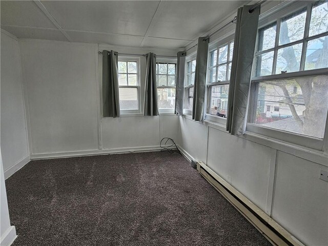 unfurnished room featuring baseboard heating, a wealth of natural light, and dark colored carpet