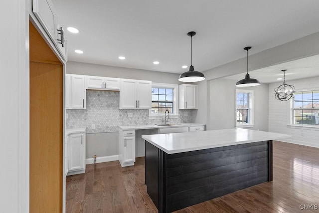 kitchen featuring dark wood-style floors, backsplash, a center island, hanging light fixtures, and white cabinetry