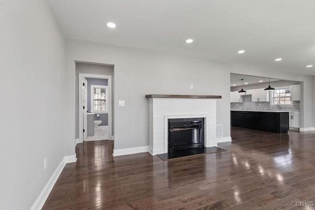 unfurnished living room featuring a fireplace with flush hearth, visible vents, a sink, baseboards, and dark wood-style flooring