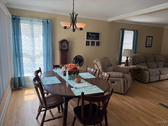 dining room with light wood-type flooring, visible vents, an inviting chandelier, and crown molding